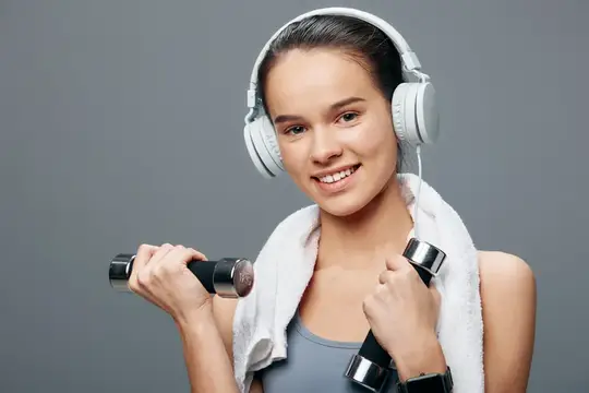 Улыбающаяся девушка с гантелями и в наушниках после тренировки