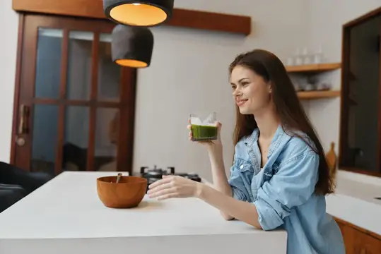 Улыбающаяся темноволосая девушка с зелёным смузи на светлой кухне