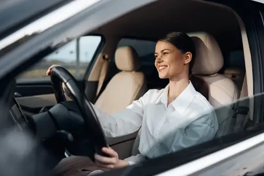 Улыбающаяся женщина в белой рубашке за рулём автомобиля