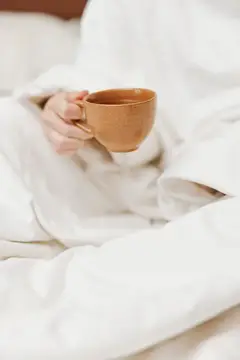 Человек с чашкой кофе и одеялом лежит в кровати, чтобы согреться
