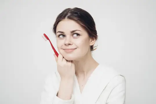 Молодая женщина с красной зубной щеткой улыбается на белом фоне
