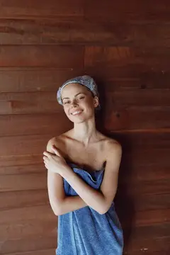 Улыбающаяся девушка в полотенце и шапочке для душа на фоне деревянной стены