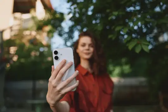 Девушка в красной рубашке делает селфи на смартфон летом