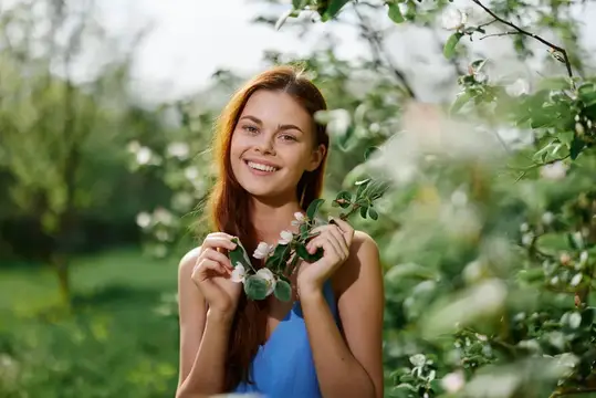 Портрет женщины, которая красиво улыбается, обнажая зубы, излучая весеннее счастье на фоне зеленого дерева