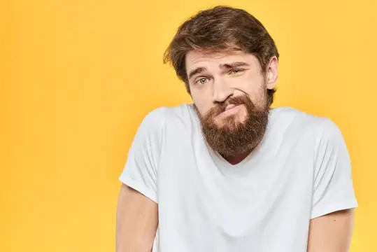 Бородатый мужчина в белой футболке жестикулирует руками, демонстрируя эмоции