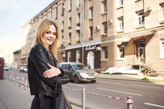 Модная женщина в кожаной куртке позирует на улице возле здания