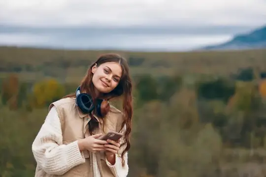 Молодая девушка с наушниками и телефоном на фоне осенних холмов