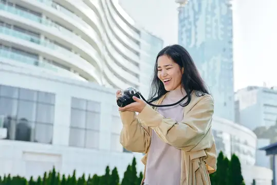 С фотоаппаратом в руках улыбающаяся женщина наслаждается уличной городской фотосъемкой при дневном свете