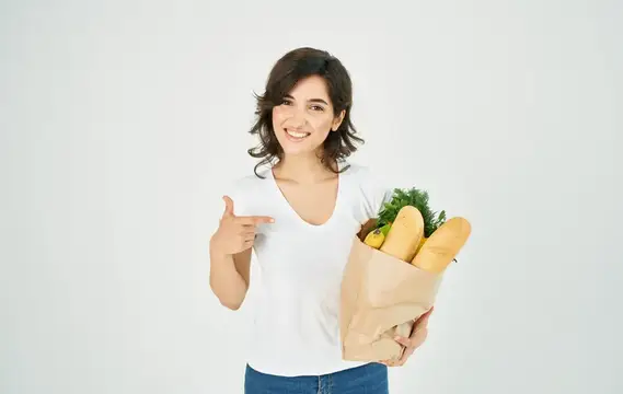 Улыбающаяся брюнетка с бумажным пакетом продуктов показывает на него пальцем