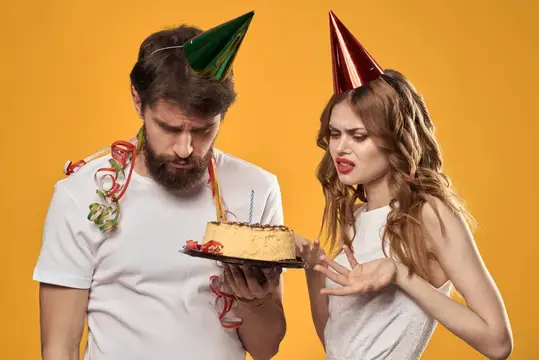 Удивлённые мужчина и женщина в колпаках с тортом на жёлтом фоне