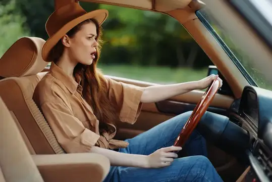 Молодая женщина в шляпе и рубашке ведет автомобиль
