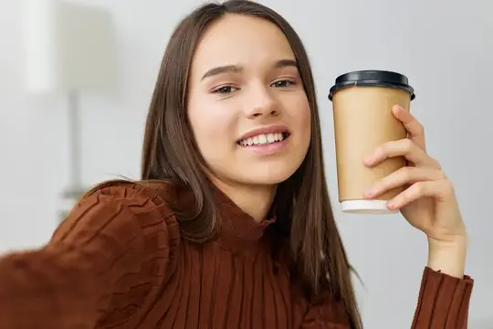 Улыбающаяся девушка с бумажным стаканом кофе дома