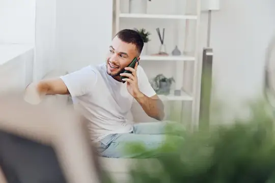Улыбающийся мужчина с комфортом сидит и ведет душевный телефонный разговор, воплощая темы мужской уязвимости и культуры терапии