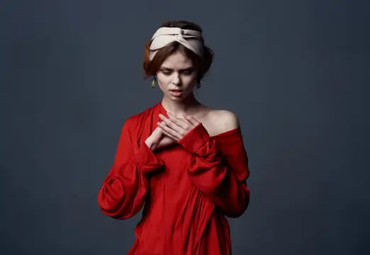 Молодая женщина в красном платье с повязкой на голове на тёмном фоне