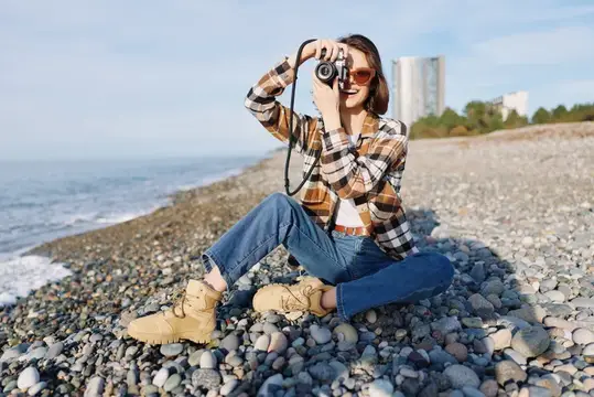 Девушка в клетчатой рубашке фотографирует на камеру у моря