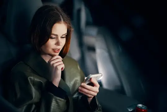 Задумчивая девушка со смартфоном в тёмном салоне автомобиля