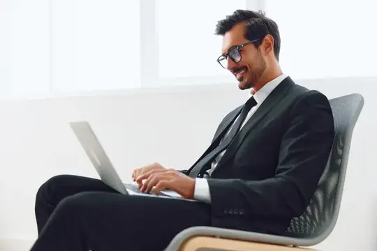 Улыбающийся мужчина в очках и костюме работает за ноутбуком в кресле