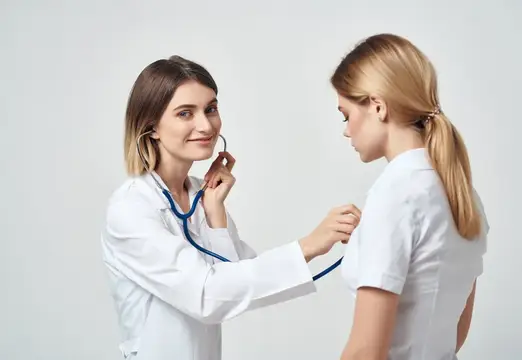 Женщина-врач в белом халате слушает пациентку стетоскопом