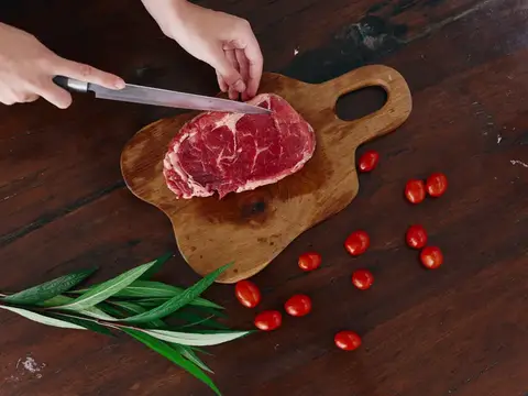 Руки нарезают кусок сырого мяса на деревянной доске