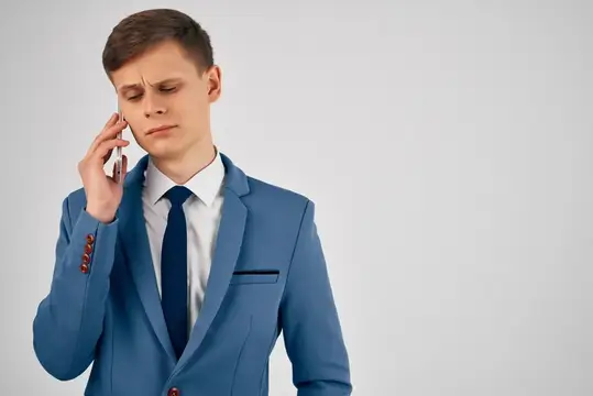 Молодой человек в синем костюме хмурится во время телефонного разговора