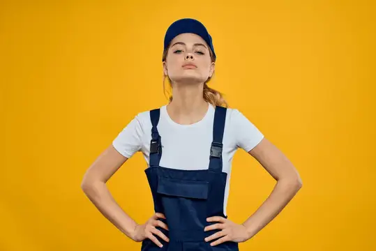 Уверенная девушка в синем комбинезоне и кепке на жёлтом фоне