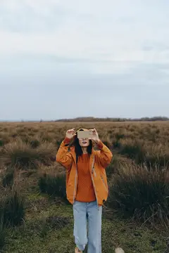 Девушка в оранжевой куртке фотографирует на телефон сухое поле