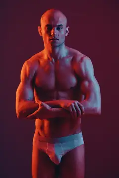 Мускулистый лысый мужчина в белых плавках на тёмном фоне