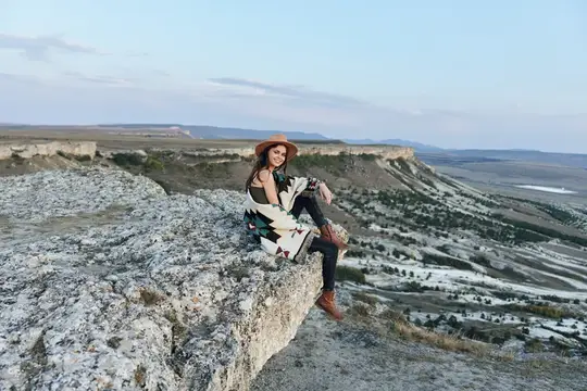 Женщина в шляпе сидит на камне, глядя на величественную долину и горы