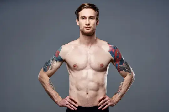 Спортивный мужчина с татуировками на руках, обнажённый торс, культурист на сером фоне