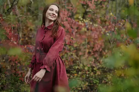 Улыбающаяся девушка в бордовом платье среди осенних кустов