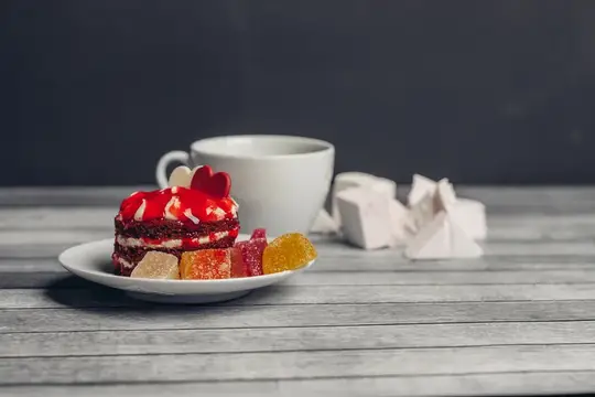 Чашка чая и красное пирожное на блюдце, сладости, десерт на деревянном фоне