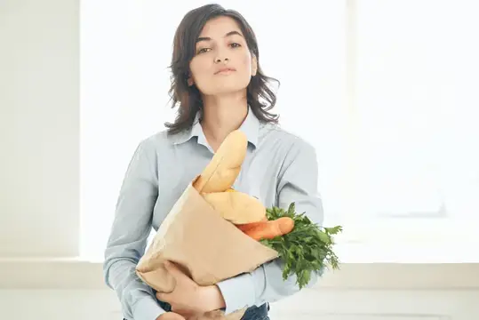 Женщина в семейной одежде держит пакет с продуктами здорового питания и домашними заданиями