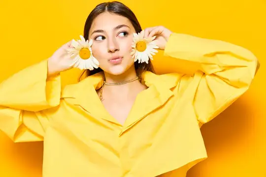 Молодая девушка в жёлтом пиджаке с ромашками у лица на жёлтом фоне