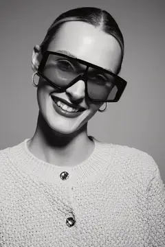 Улыбающаяся девушка в больших солнцезащитных очках на сером фоне