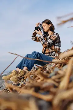 Молодая женщина фотографирует на плёночную камеру, сидя на сухой траве