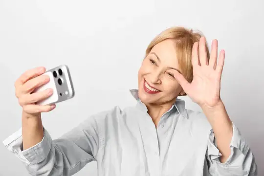 Улыбающаяся блондинка делает селфи и машет рукой на светлом фоне