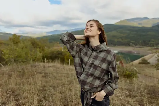 Красивая женщина в клетчатой рубашке наслаждается безмятежной природой, стоя у горного озера в туристическом направлении