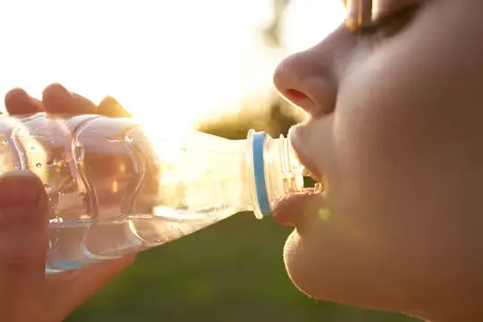 Девушка пьёт воду из бутылки на закате