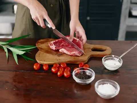 Женщина с ножом в руке нарезает стейк из мяса для жарки на кухне