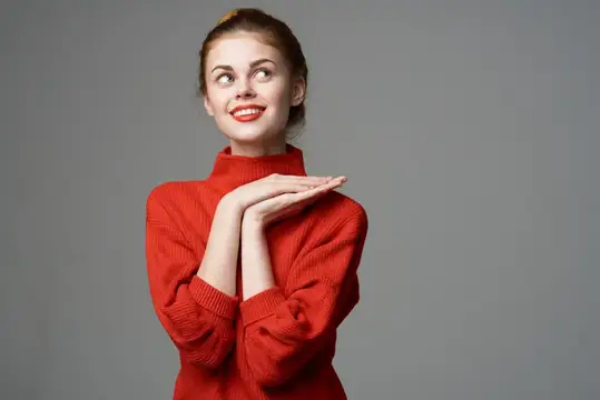 Счастливая женщина в красном свитере на сером фоне жестикулирует руками, эмоции, идея, мечтания