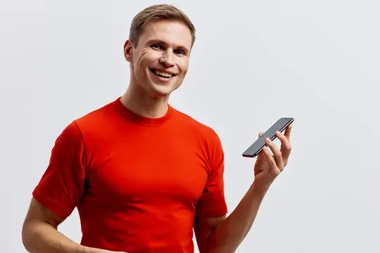 Улыбающийся парень в красной футболке держит смартфон