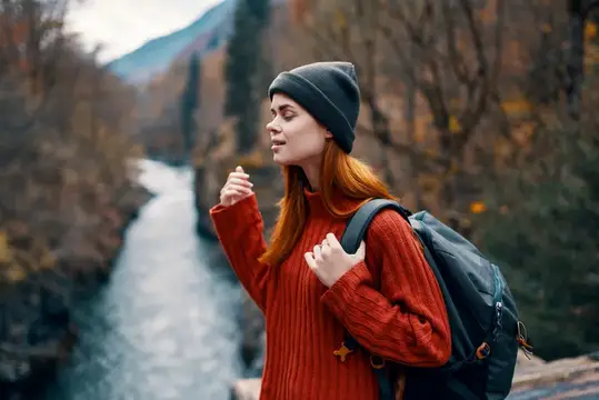 Женщина-туристка с рюкзаком на мосту у реки, осенний лес, горы