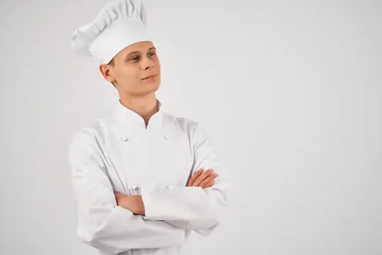 Молодой повар в белом колпаке и кителе со скрещёнными руками