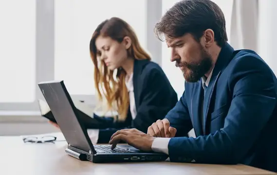 Бородатый мужчина в костюме работает за ноутбуком в офисе