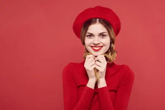 Улыбчивая девушка в красном берете и свитере на красном фоне