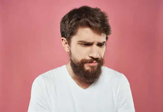 Задумчивый бородатый мужчина в белой футболке на розовом фоне