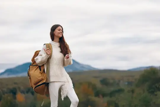 Улыбающаяся девушка с рюкзаком гуляет по осенним холмам