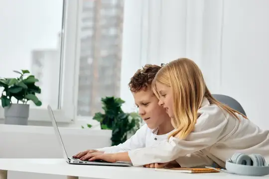 Мальчик и девочка вместе смотрят в ноутбук у окна