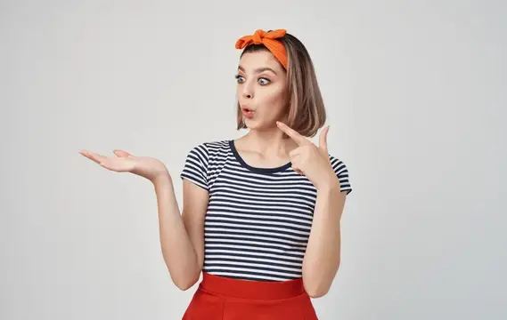 Молодая женщина с оранжевым бантом удивлённо жестикулирует на светлом фоне