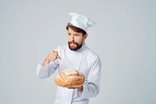 Бородатый мужчина-шеф-повар на кухне с хлебобулочными изделиями на светлом фоне